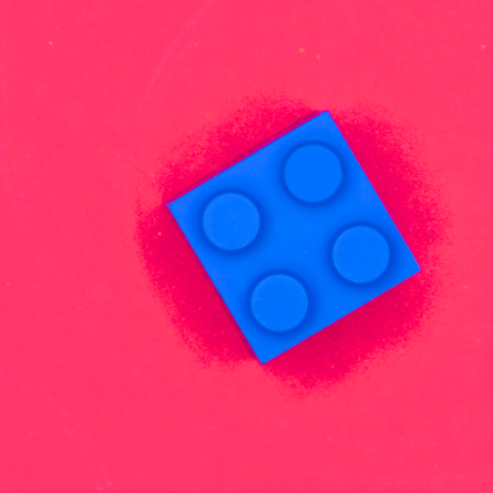 Bright rose-red background and a single square blue LEGO piece positioned to the right