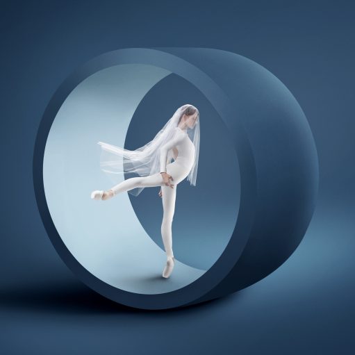 A ballerina en pointe dressed in all white standing in a sculptural wheel highlighting the beauty and drama represented by the Philadelphia Ballet.