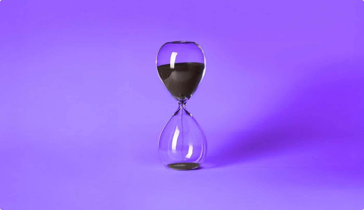 Clear glass hourglass with black sand partially emptied, set against a vibrant purple background.