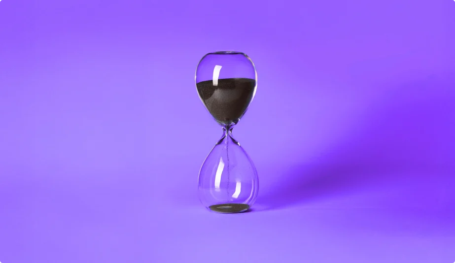 Clear glass hourglass with black sand partially emptied, set against a vibrant purple background.
