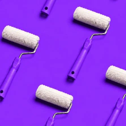 White paint rollers with purple handles arranged in a diagonal pattern on a purple background.