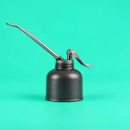 Dark metal oil can with a long silver spout on a mint green background.