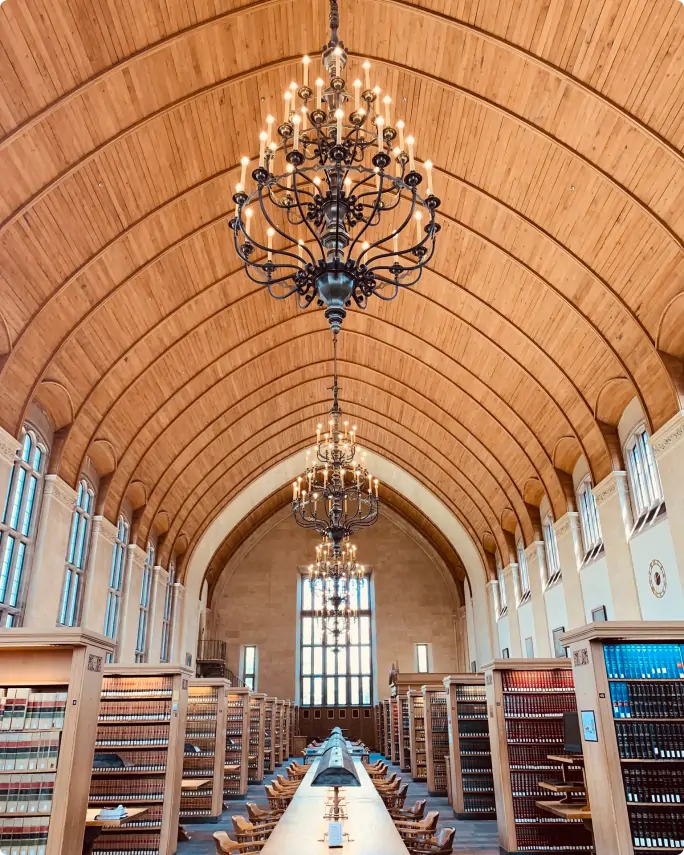 the inside of the Cornell Law library with chandelier, book shelves, long table in the center, and high windows