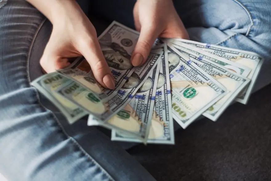 a pair of hands holding several fanned out $100 bills