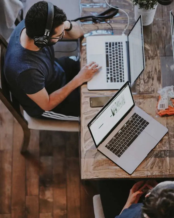 an overhead shot of a man working on his laptop and another laptop next to him