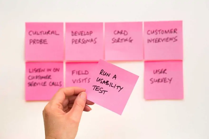 a man's hands holding a stickie note that says run a usability test while in the background are notes with other steps in the process such as cultural probe, card sorting, and user survey