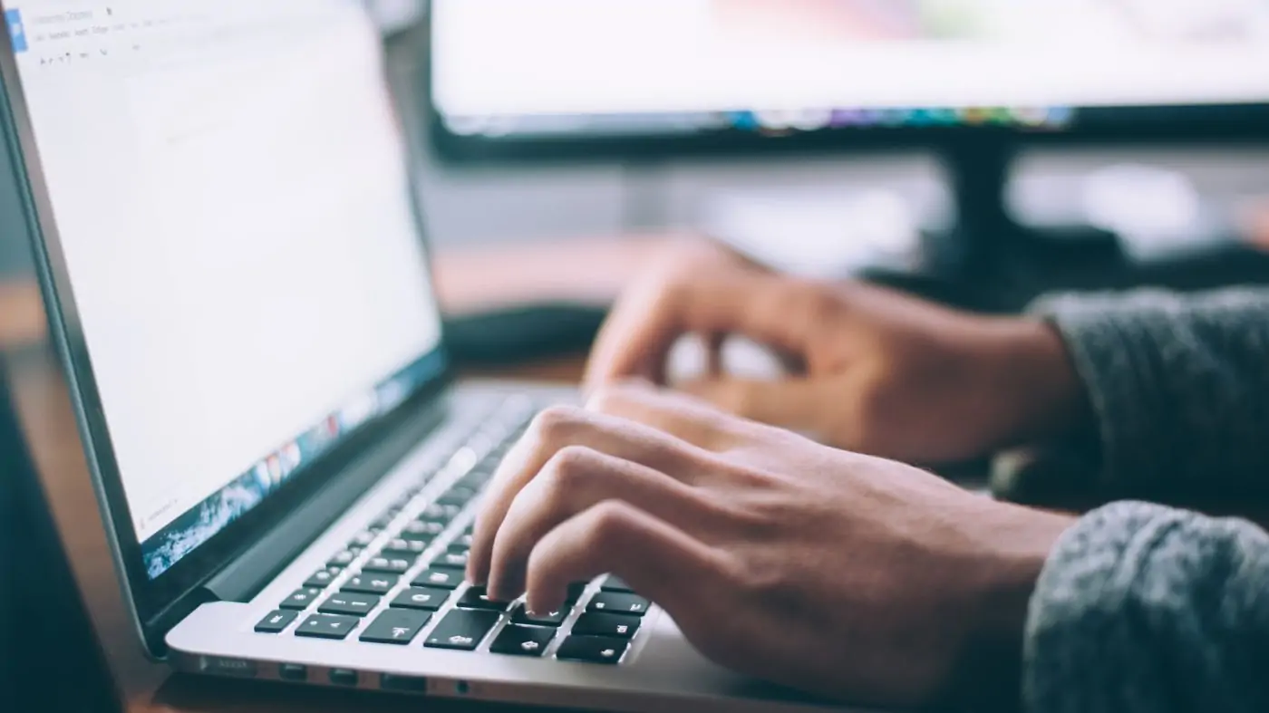 a man's hands typing on a laptop with a blank screen