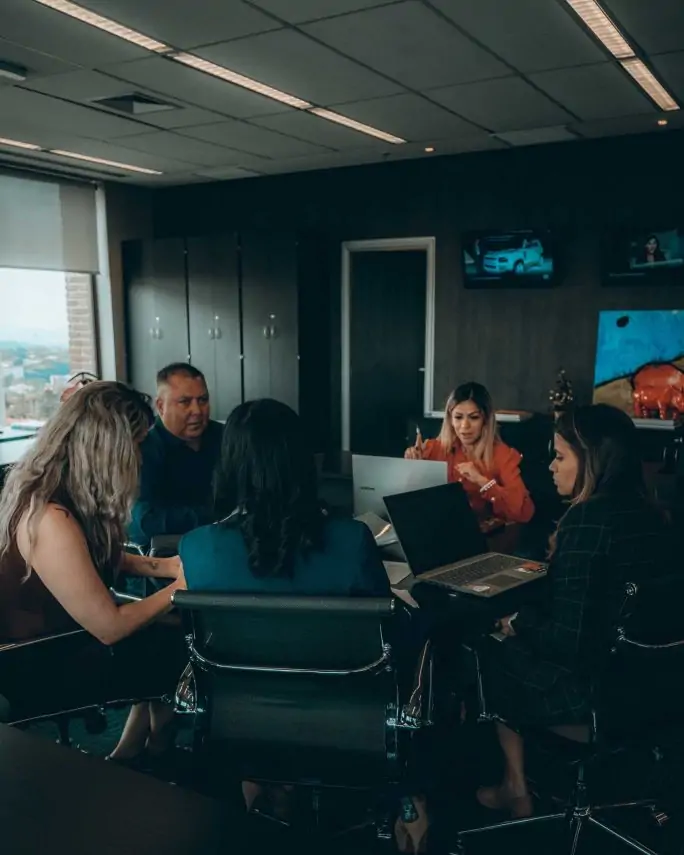 four women and one man working at a table in a dim conference room