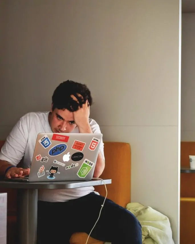 a male college student bent over his laptop looking distressed