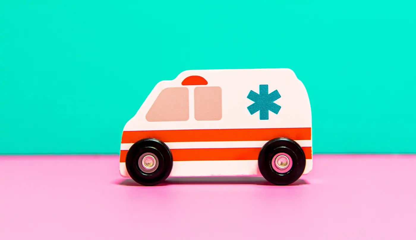 A charming wooden toy ambulance placed at the center of the image on a delightful pink ground with a mint green backdrop.