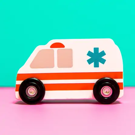 A charming wooden toy ambulance placed at the center of the image on a delightful pink ground with a mint green backdrop.