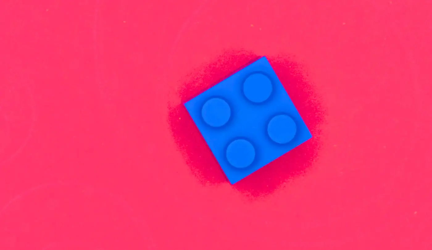 Bright rose-red background and a single square blue LEGO piece positioned to the right