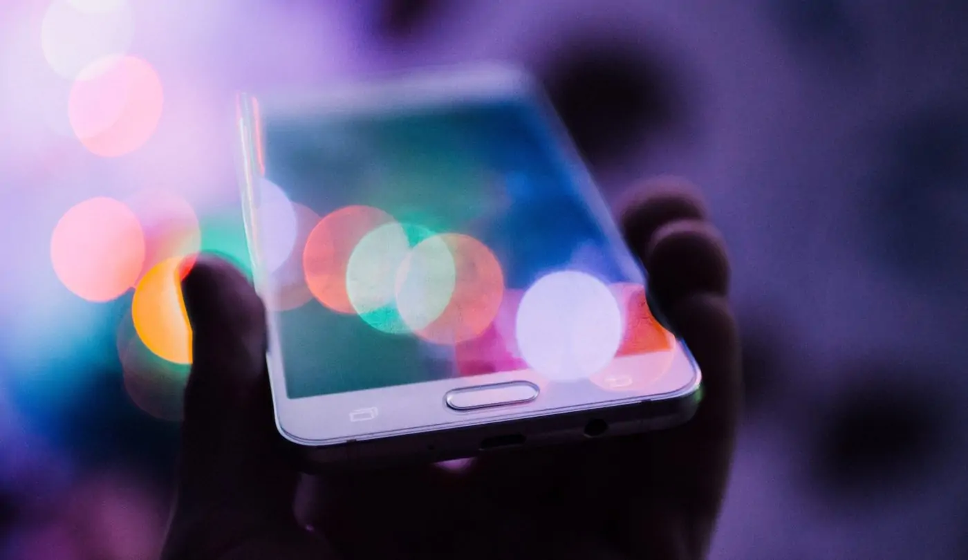 Colorful image of a person's hand holding a smartphone, with a captivating lens flare effect illuminating over the photo.