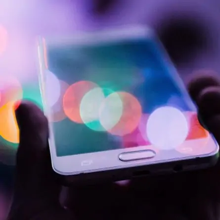 Colorful image of a person's hand holding a smartphone, with a captivating lens flare effect illuminating over the photo.