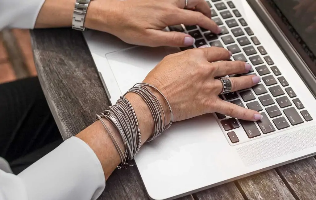 a woman's hands typing on a laptop keyboard and a notebook and pen next to her