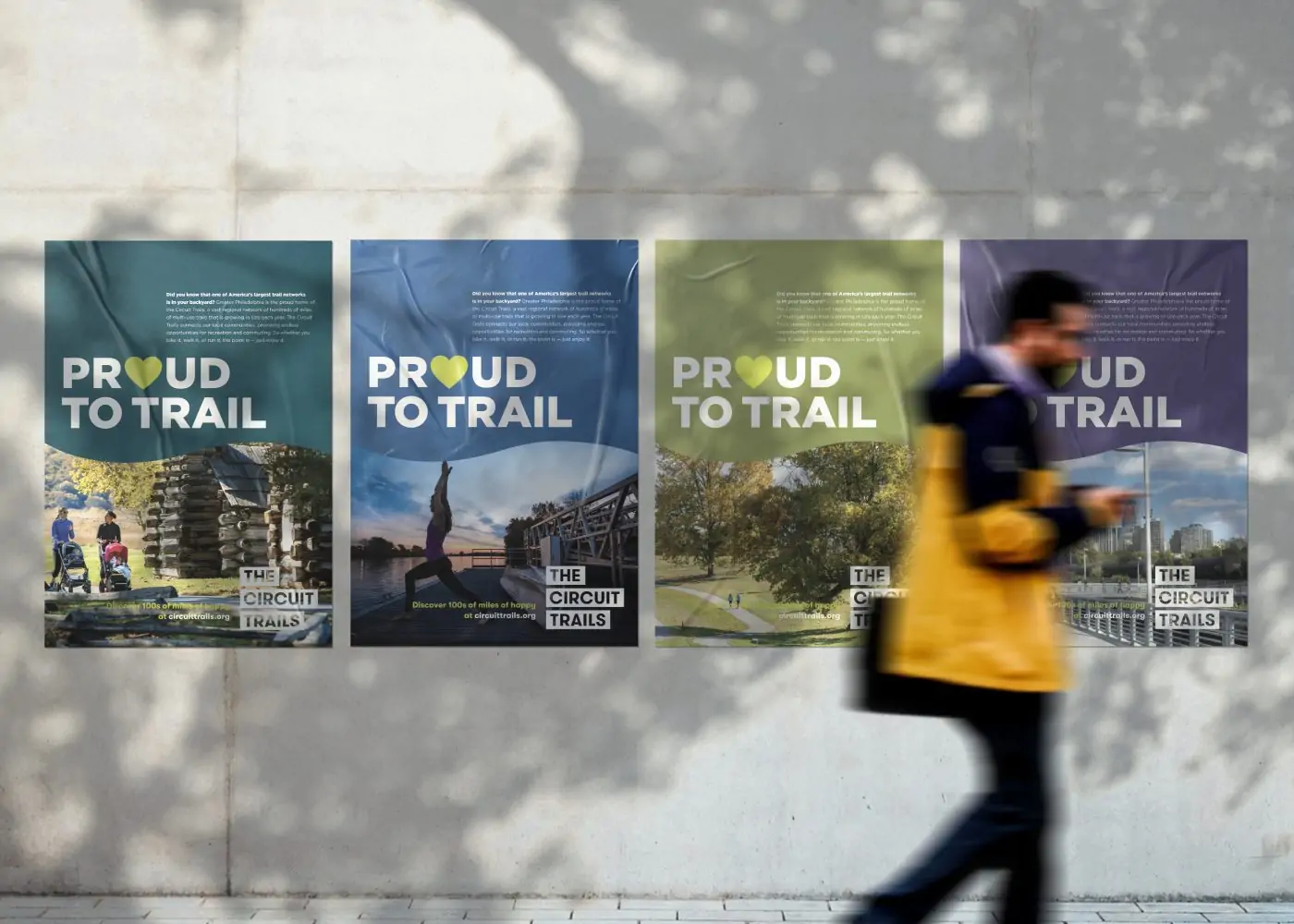 A city block shows a man walking by 4 posters on a wall that say 