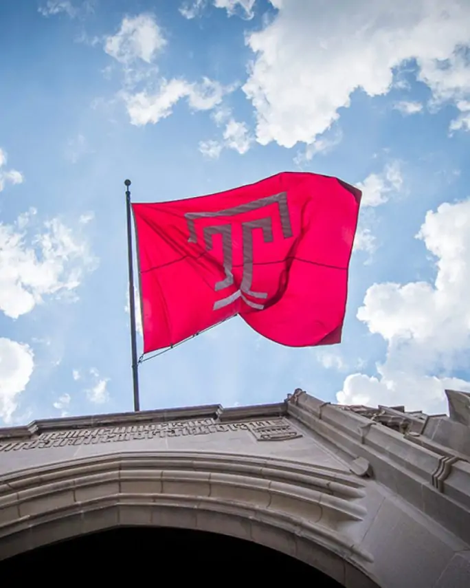 Red temple flag wtih bold white T logo flying in the wind mounted on a campus building