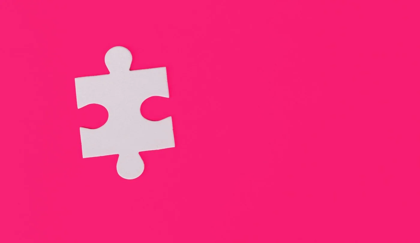 A white puzzle piece on a pink background