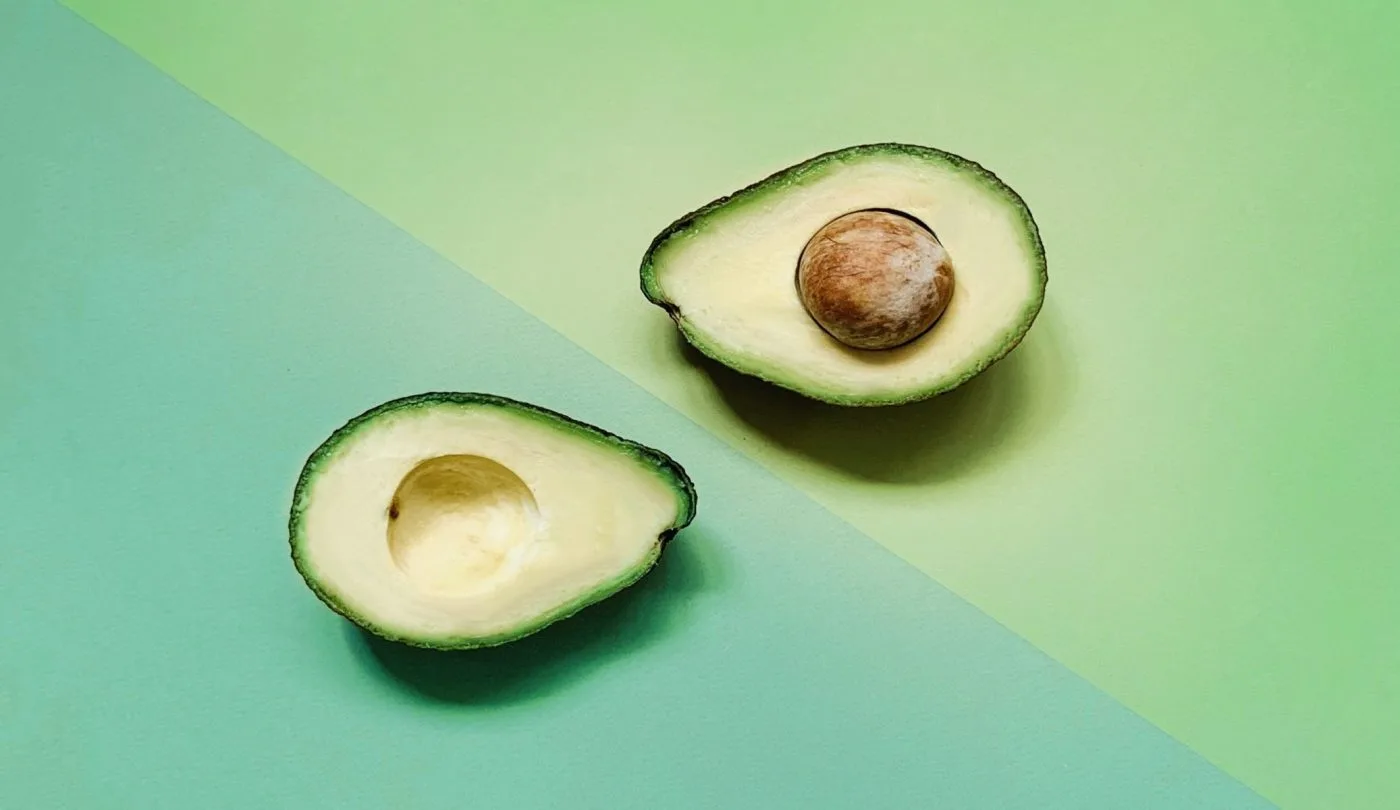 Avocado divided into two halves, with two a triangle with a different shade of green color as its background.