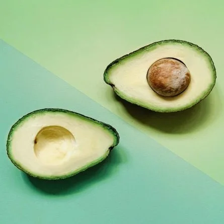 Avocado divided into two halves, with two a triangle with a different shade of green color as its background.